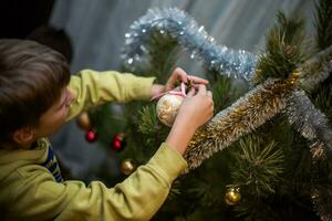 A boy decorates a natural pine tree with simple kraft toys. Real life photo