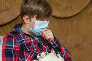 boy in protective medical mask lies in bed and coughs. Kid child is sick. child with influenza or cold protected from viruses among patients with coronavirus. photo