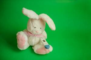 Toy Hare with electronic thermometer under paw. Measuring high temperature of children with influenza and viruses, coronavirus. Medicine concept. photo