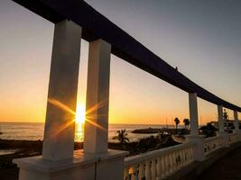 the sun is setting over the ocean and a bridge photo