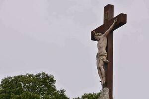 un estatua de Jesús en un cruzar con arboles en el antecedentes foto