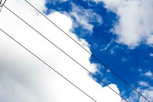 Electric wires against sky. White fluffy clouds in blue sky in summer. Background with cloud. photo
