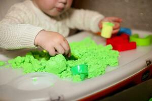 niña obras de teatro con cinético arena. niño construye pastores en formar de letras de arena. temprano desarrollo de niños. multa motor habilidades de el dedos. foto