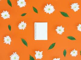 Directly above view of blank notebook with white flowers and green leafs on orange background. photo