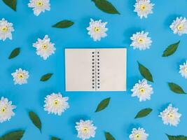 Directly above view of blank notebook with white flowers and green leafs on blue background. photo