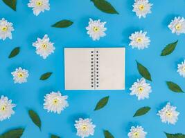 directamente encima ver de blanco cuaderno con blanco flores y verde hojas en azul antecedentes. foto