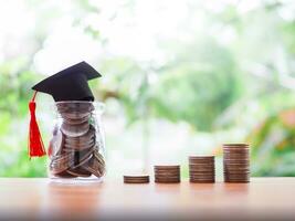 Glass bottle with graduation hat and stack of coins. The concept of saving money for education, student loan, scholarship, tuition fees in future photo