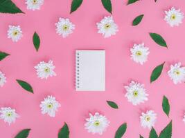 Directly above view of blank notebook with white flowers and green leafs on pink background. photo