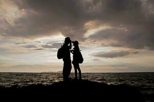 silueta de Pareja en pie en el playa a puesta de sol foto