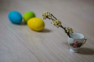 Three Easter eggs near a cup with a sprig of plum. Easter background for mobile and computer screens. photo