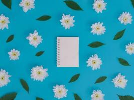 Directly above view of blank notebook with white flowers and green leafs on blue background. photo