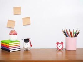 Office desk table, Student creative desktop with colorful stationery, hardcover book, sticky notes. Piggy bank with graduation hat. Copy space for text, Back to school, Education concept photo