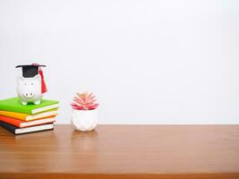 Piggy bank with graduation hat on hardcover book and potted cactus. Copy space for text, Back to school, Education concept photo
