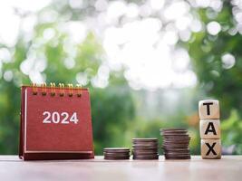 Close up 2024 desk calendar, Wooden blocks with the word TAX and stack of coins, The concept of saving money for payment tax in New Year 2024 photo