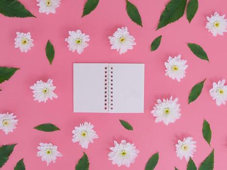 Directly above view of blank notebook with white flowers and green leafs on pink background. photo