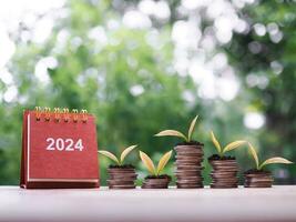 2024 desk calendar, Plants growing up on stack of coins. The concept of saving money, Financial, Investment and Business growing in new year 2024. photo