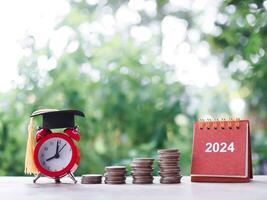 Study goals, 2024 Desk calendar, Red alarm with graduation hat and stack of coins. The concept of saving money for education, student loan, scholarship, tuition fees in New Year 2024 photo