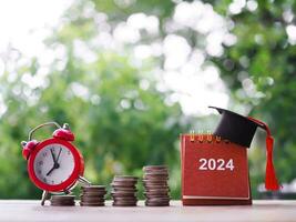 Study goals, 2024 Desk calendar with graduation hat and red alarm on stack of coins. The concept of saving money for education, student loan, scholarship, tuition fees in New Year 2024 photo