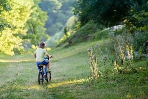 The little boy in a striped suit goes on a forest road. Child in a protective bicycle helmet riding a blue bike. photo