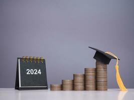 Study goals, 2024 Desk calendar, Graduation hat on stack of coins. The concept of saving money for education, student loan, scholarship, tuition fees in New Year 2024 photo