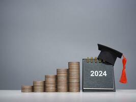 Study goals, 2024 Desk calendar with graduation hat and stack of coins. The concept of saving money for education, student loan, scholarship, tuition fees in New Year 2024 photo