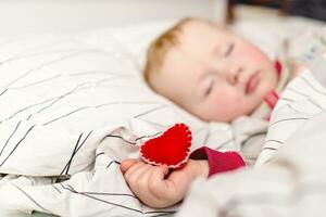 niño duerme y sostiene en mano juguete corazón de sintió. contento madre día concepto foto