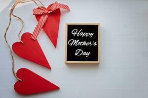 HAPPY MOTHER'S DAY Three red wooden hearts around around wooden frame with black background. top view with copy space photo