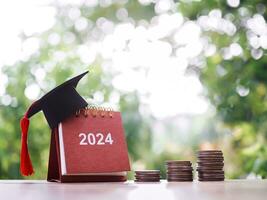 Study goals, 2024 Desk calendar with graduation hat and stack of coins. The concept of saving money for education, student loan, scholarship, tuition fees in New Year 2024 photo