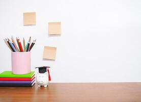 Office desk table, Student creative desktop with colorful stationery, hardcover book, sticky notes. Piggy bank with graduation hat. Copy space for text, Back to school, Education concept photo