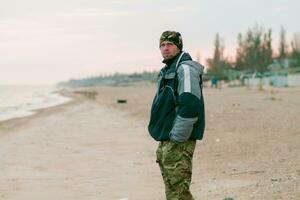 A young man in camouflage turned. A man stands on the beach in s photo