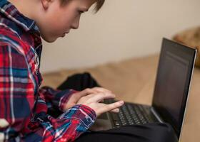 boy in plaid shirt does lessons on laptop. child learns remotely during quarantine of coronavirus. Online learning from home. photo