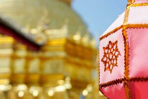 Closeup Thai Lanna style lanterns to hang in front of the golden pagoda at Thai temple under blue sky background. photo