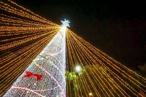 Mira arriba ver borroso y bokeh de Navidad árbol Encendiendo en noche hora antecedentes. foto