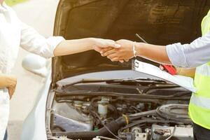 Closeup and crop of a congratulatory handshake of insurance employee and customer with sun flare on car engine background. photo