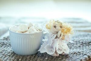 homemade angel doll with folded hands in prayer next to cup of coffee or cocoa in background of window. angel figure stands on knitted napkin on table. photo