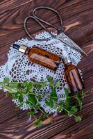 Glechoma hederacea, ground-ivy, gill-over-the-ground, creeping charlie, alehoof, tunhoof, catsfoot, creeping jenny. Cosmetic bottle of oil for body care. Essential oil in a cosmetic bottle on a wooden table. photo