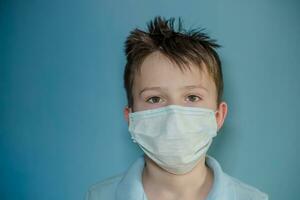 boy in medical mask on blue background. child with flu, influenza or cold protected from viruses, pollution in bad epidemic situation, among patients with coronavirus photo