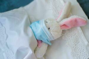 Rabbit in a protective medical mask lies in a crib on a white bed. The toy got sick. Playing doctor. Protection from viruses, influenza, coronavirus for children. photo