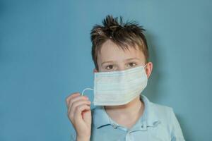 Boy teen takes off medical mask on blue background. child with flu, influenza or cold protected from viruses, pollution in bad epidemic situation, among patients with coronavirus photo