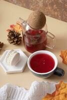 Cup and glass teapot with cranberry tea and macaroon with an autumn leaf. Autumn warm drink concept photo