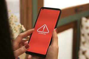 woman using smartphone with warning triangle showing a system error. Concepts of system maintenance, security, anti-virus, and anti-hacking access to critical data. photo