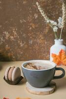 A cup of warm cocoa with a macaroon and cozy autumn decor. Fall still life with a warm drink photo