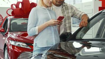 Pareja utilizando inteligente teléfono mientras comprando un nuevo coche video