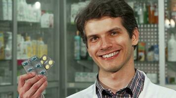 Cheerful male chemist smiling holding two blisters of pills video