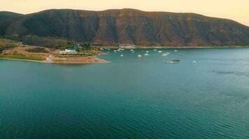 Aerial drone flying over a lake, water dam, with mountains, and boats on coastline, at sunrise. Beautifull dreamy landscape view. video