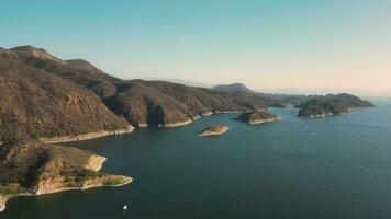 aéreo zumbido volador terminado un lago, agua presa, con montañas a amanecer. hermoso soñador paisaje vista. video