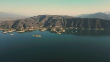 Aerial drone flying over a lake, water dam, with mountains, and boats on coastline, at sunrise. Beautifull dreamy landscape view. video