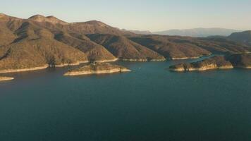 aérien drone en volant plus de une lac, l'eau barrage, avec montagnes à lever du soleil. beau rêveur paysage voir. video