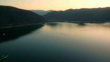 aérien drone en volant plus de une lac, l'eau barrage, avec montagnes à lever du soleil. beau rêveur paysage voir. video