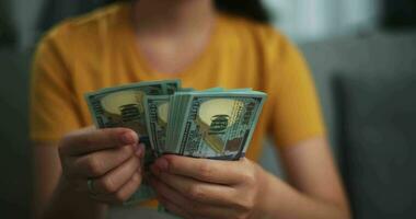 Aufnahmen schließen oben Hände von jung asiatisch Frau genießen Zählen Kasse Dollar Banknoten auf Sofa im das Leben Zimmer beim heim. video